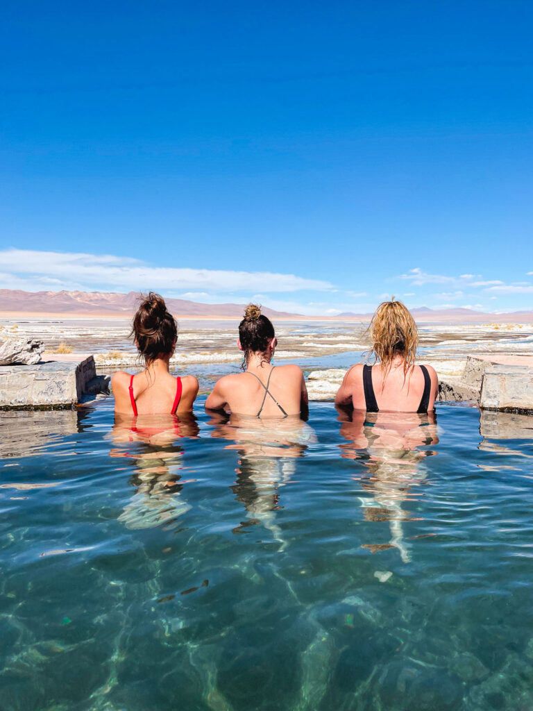 Travelers enjoying a natural hot spring in South Lipez, with views of the lagoon and Andean mountains, Bolivia.