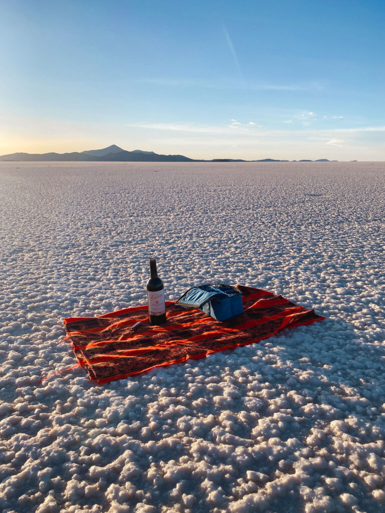Wine bottle on a blanket in Salar de Uyuni at sunset, Bolivia.