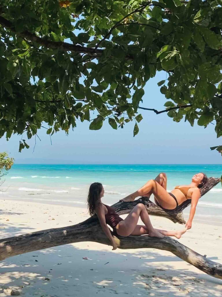 Eva and Manon on a tree trunk on a paradise beach in Havelock, Andaman and Nicobar Islands, India.