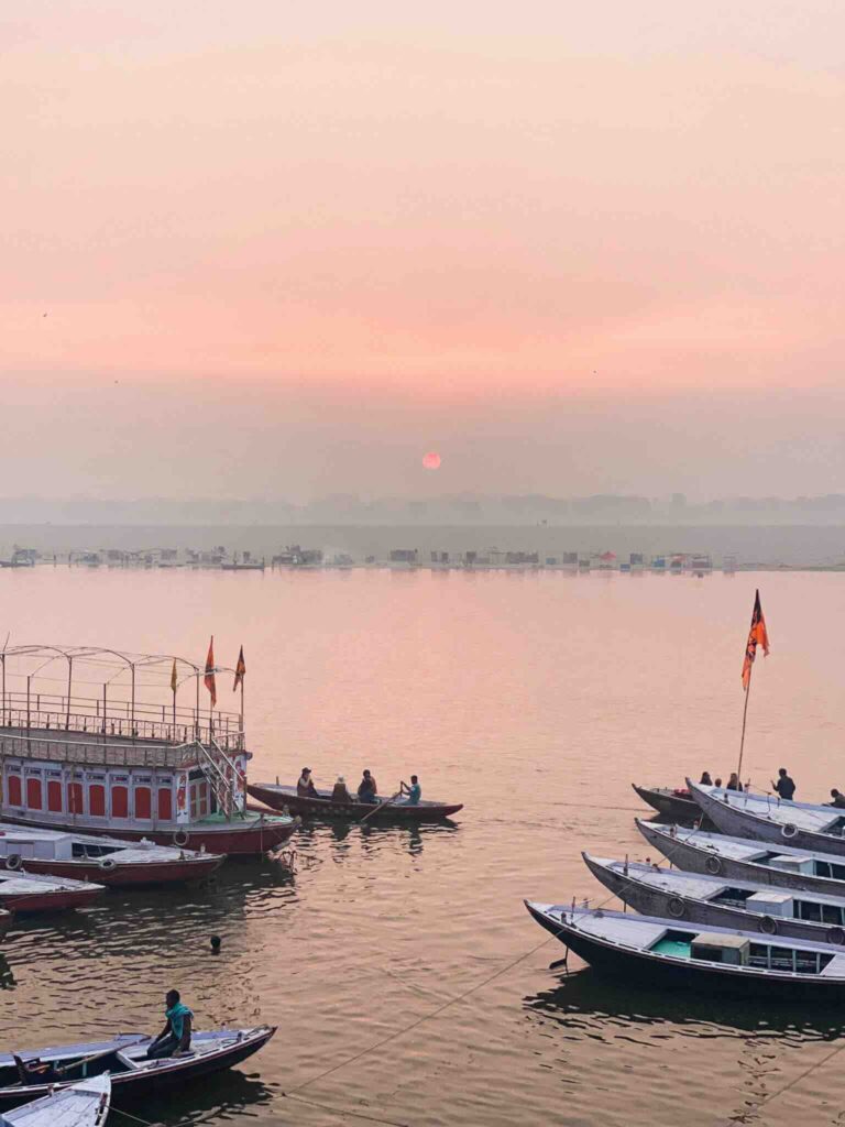 Sunrise over the Ganges in Varanasi with traditional boats and a pink sky.