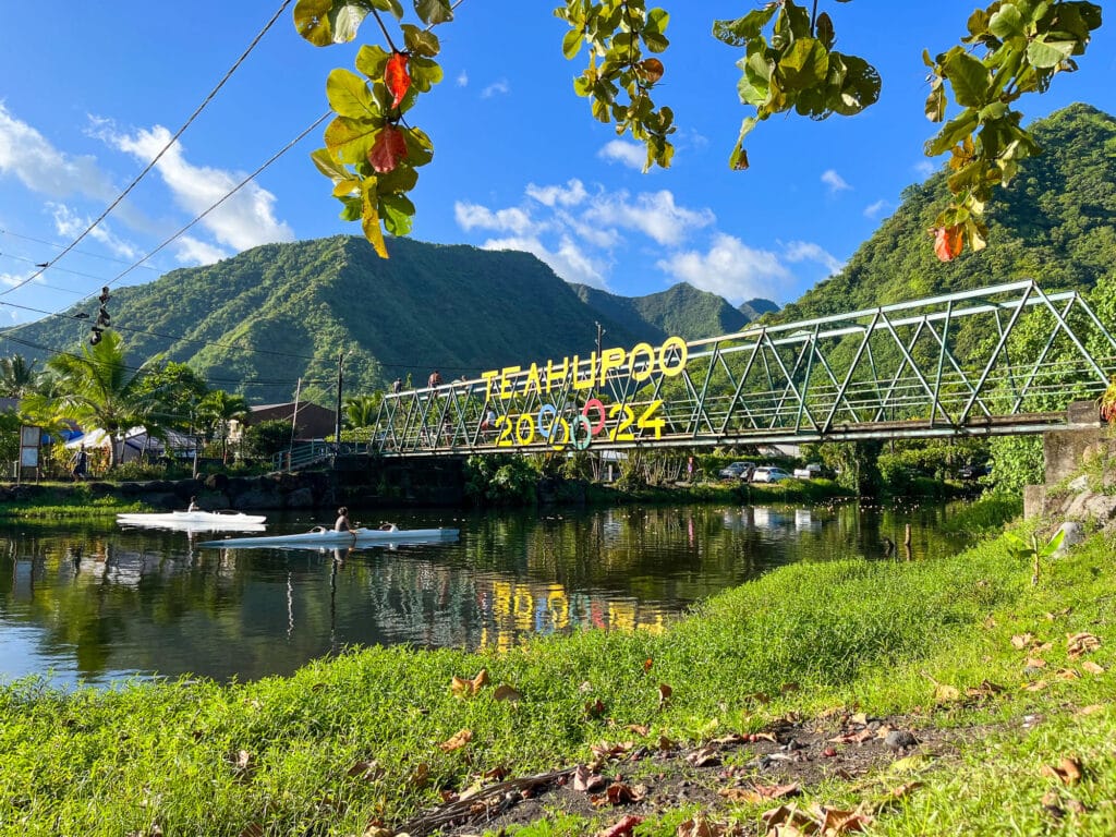 Pont de Teahupoo décoré pour les JO 2024, avec paysages tropicaux en arrière-plan.