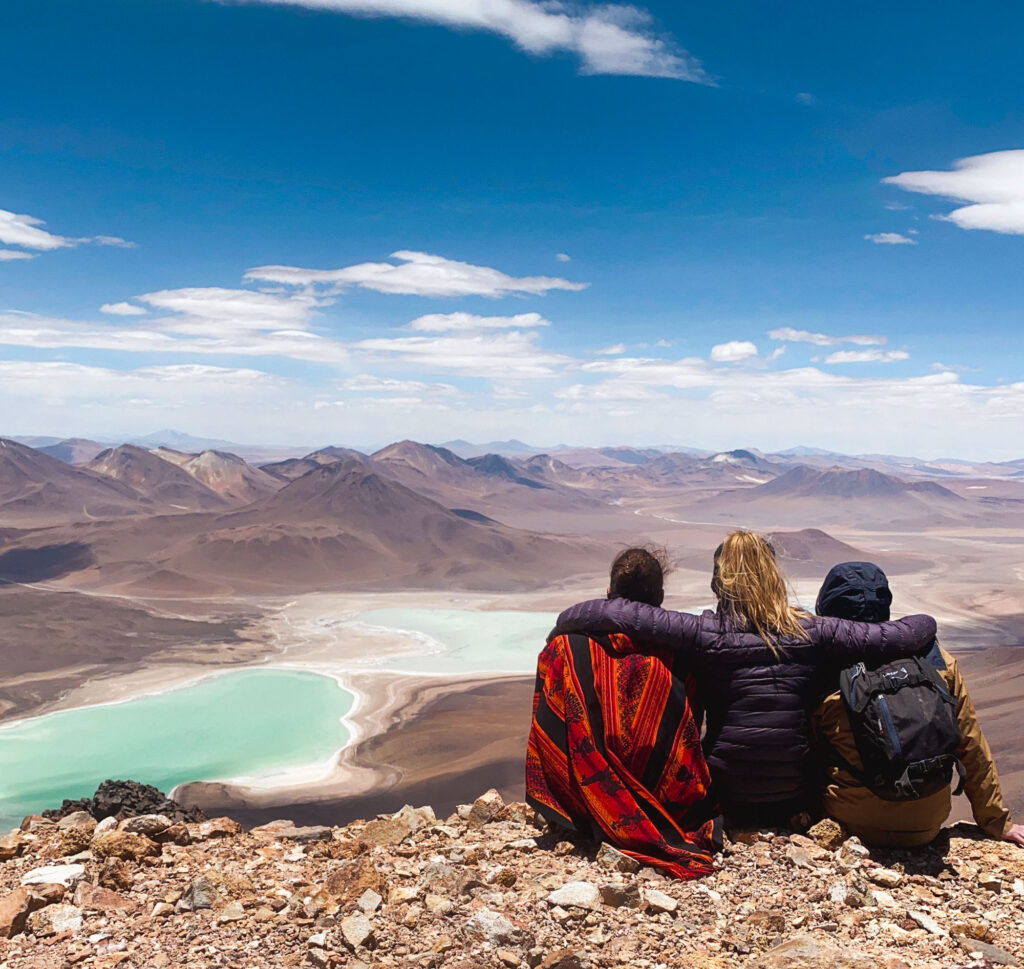 Three travelers admiring Laguna Verde and the volcanoes of Sud Lipez from the summit of Mount Licancabur, Bolivian Altiplano, Bolivia.