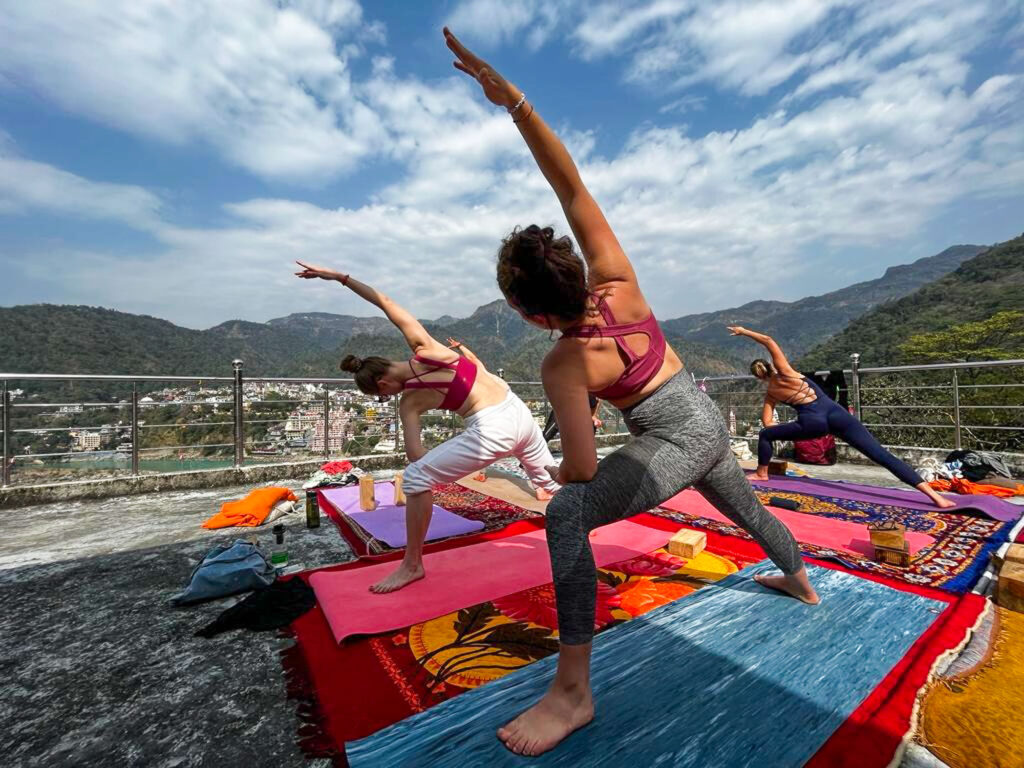 Practicing yoga asanas on a rooftop with mountain views during a yoga training in Rishikesh, India
