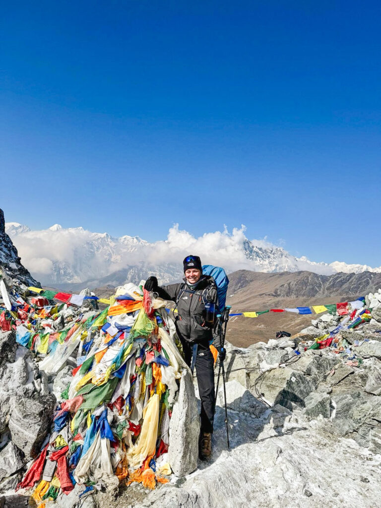 Photo at the summit of Cho La Pass with colorful prayer flags fluttering in the wind, during the Three Passes Trek in Nepal.