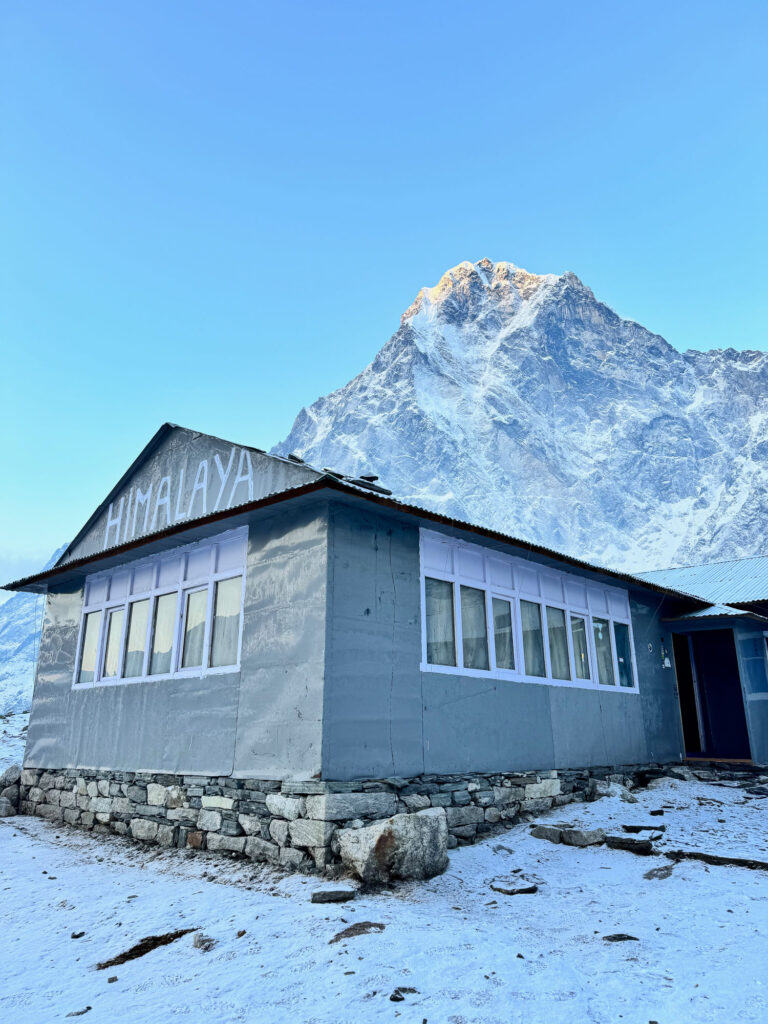 Exterior view of a Himalayan lodge with snowy landscapes and majestic mountains, during the Three Passes Trek in Nepal.