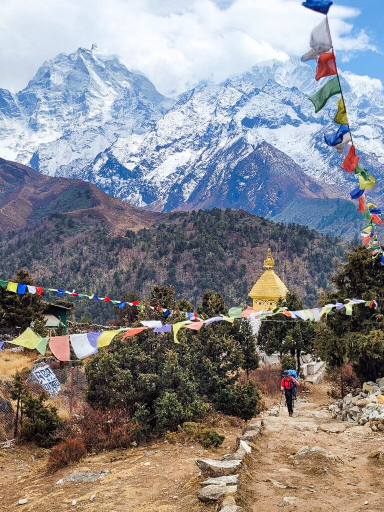 Hiker in Nepal in front of a Himalayan temple, snowy peaks and Nepali prayer flags fluttering in the wind.