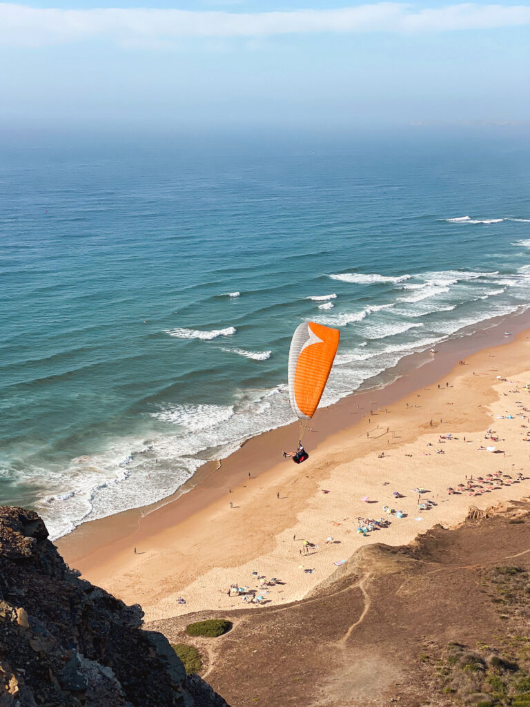 Paragliding above Miradouro do Cordoama, with views of the cliffs and ocean.