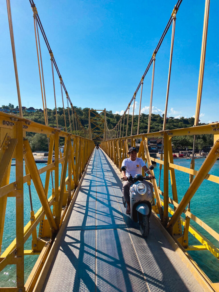 Local crossing the yellow bridge connecting Nusa Lembongan to Nusa Ceningan on a scooter.
