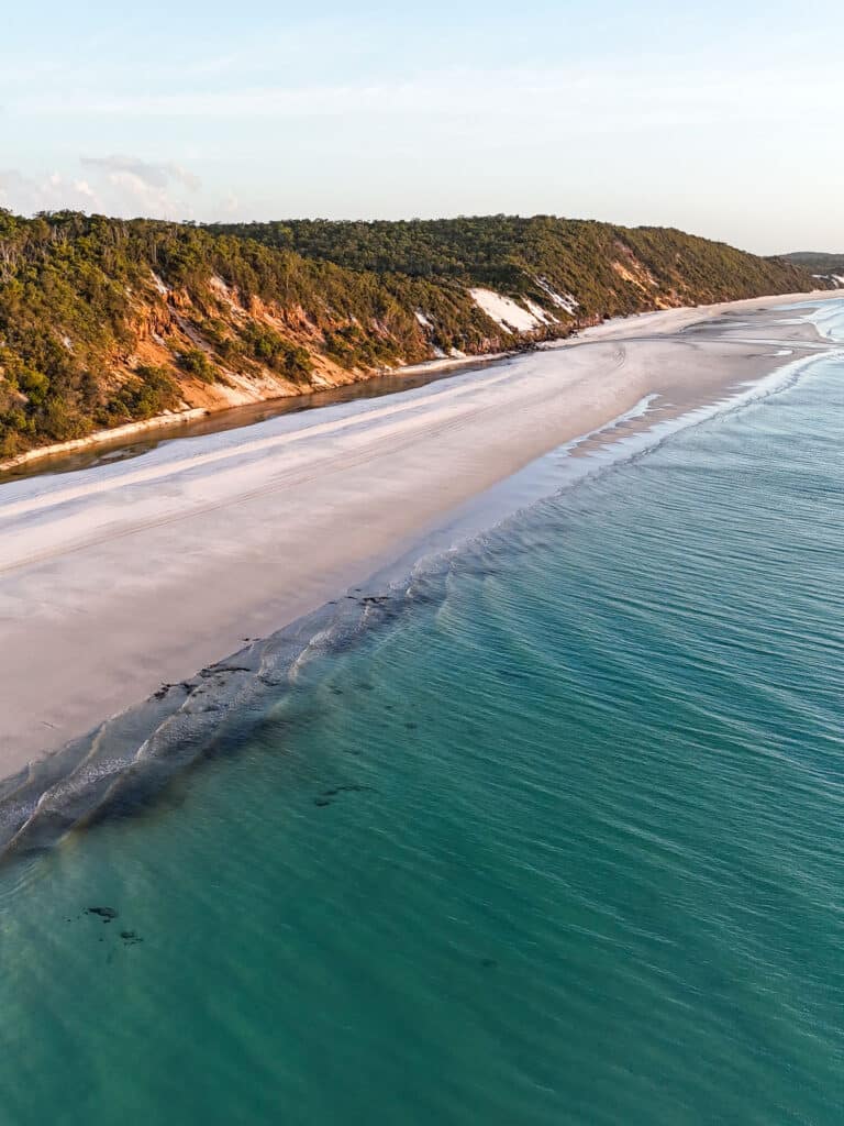 Vue drone d’une plage de Fraser Island au coucher du soleil, avec sable doré et mer calme.