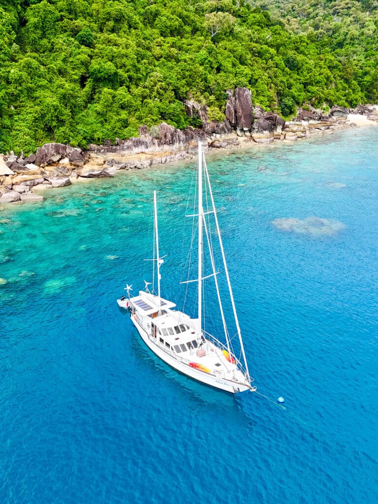 Vue drone d’un voilier ancré autour de Thomas Island, dans les Whitsundays, entouré d’eau turquoise et de végétation luxuriante lors d'un boat trip de Sydney aux Whitsundays.
