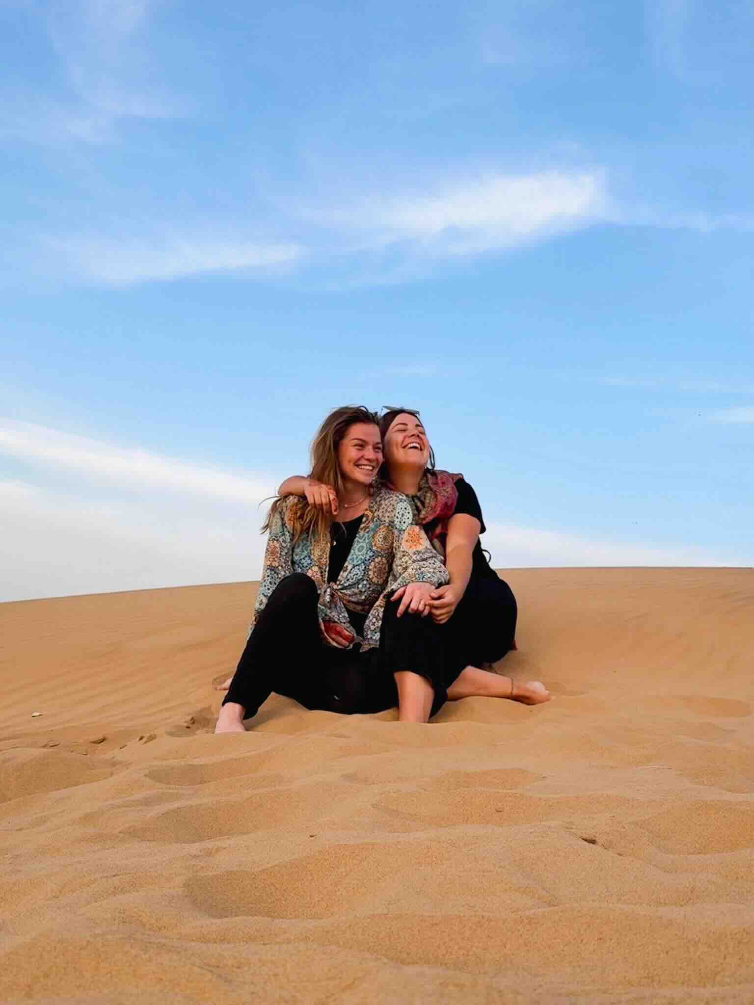 Two travel bloggers exploring the sandy desert landscape of Jaisalmer, India.